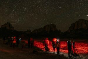 Photographers with tripods shooting the night sky under a star-filled sky surrounded by rock formations