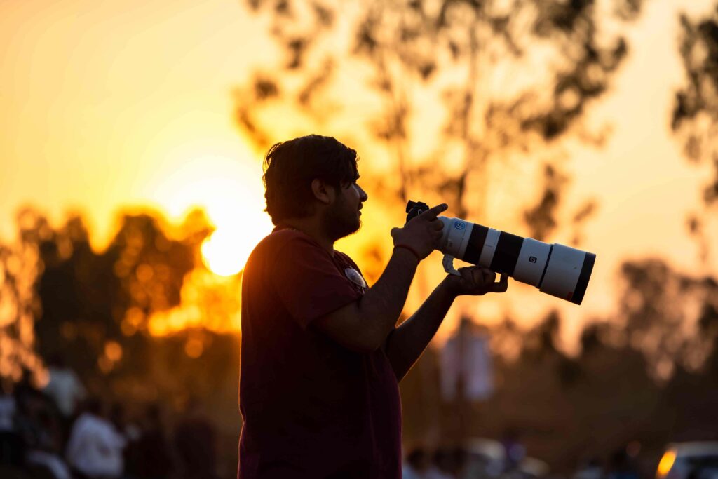 Golden Hour Photography: Tips, Techniques & How to Shoot It Right 2 - Blue Bend Photography Photographer holding a telephoto lens shooting during golden hour sunset